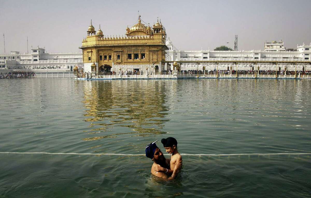 In this April 13, 2013, file photo, a Sikh man holds a child as they take a holy dip in the sacred pond at the Golden Temple, Sikhs holiest shrine, during Baisakhi festival in Amritsar, India. The chronic air pollution blanketing much of northern India is now threatening the holiest shrine in the Sikh religion, making the once-gleaming walls of the Golden Temple dingy and dull.