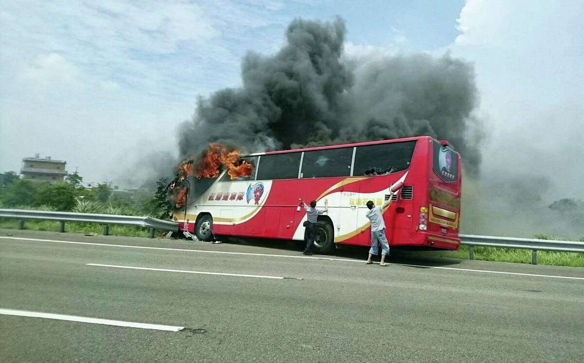 In this photo provided by Yan Cheng, a policeman and another man try to break the windows of a burning tour bus on the side of a highway in Taoyuan, Taiwan, Tuesday, July 19, 2016. Taiwanese investigators say the driver of the bus that crashed and burst into flames killing all 26 on board was driving drunk. Police coroners in Taoyuan county south of Taipei tested the driver’s blood, urine and stomach contents and found all tested for alcohol concentrations above the legal limit.