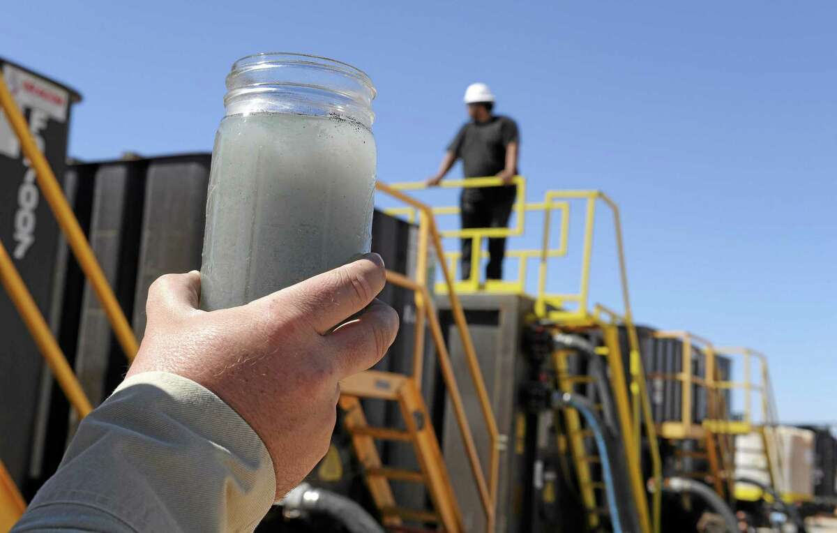 A jar holding waste water from hydraulic fracturing is held up to the light at a recycling site.