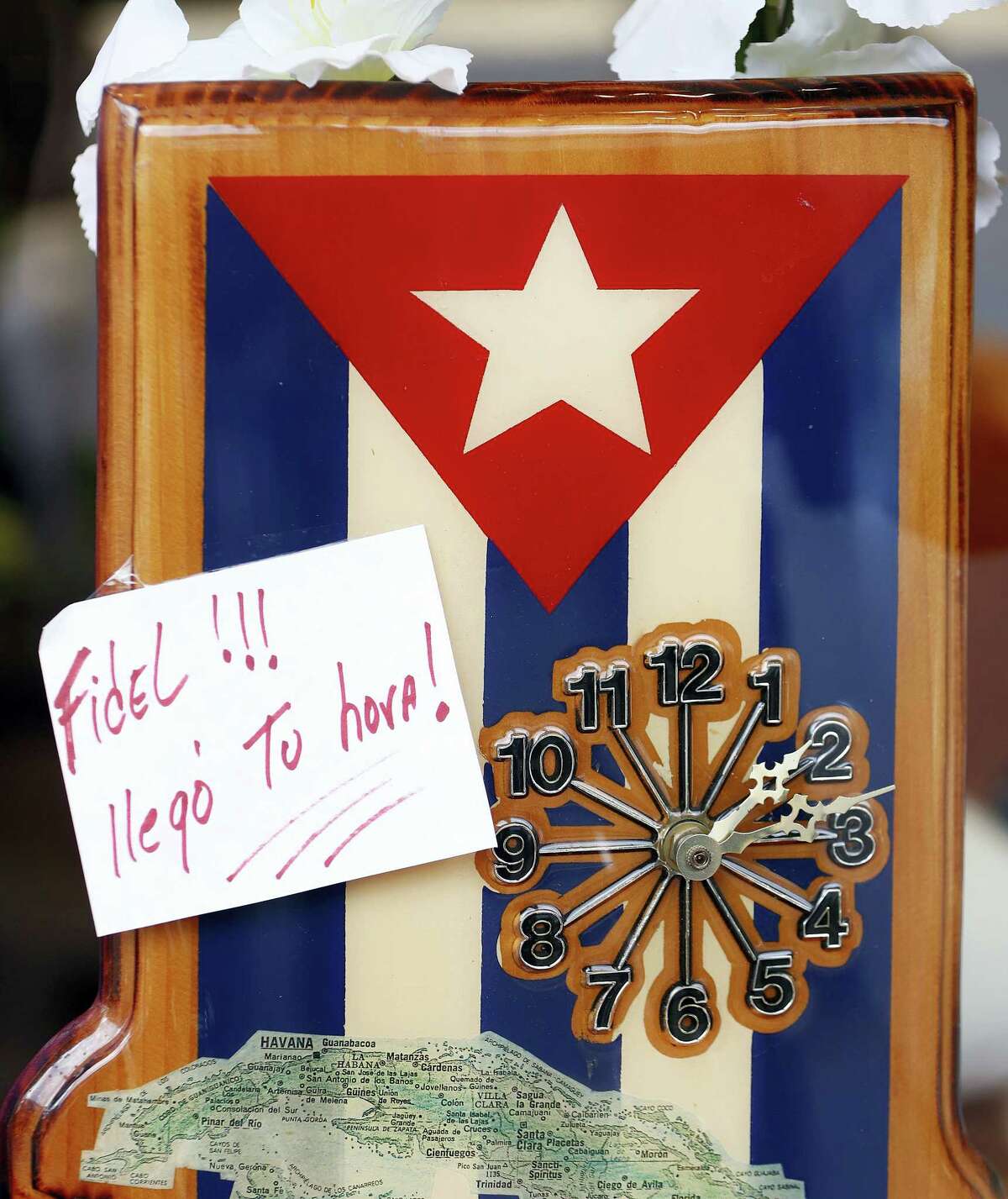 A note reading “Fidel!!! Your time has arrived” is seen on a clock with the Cuban flag at Sugarman’s Pharmacy in Union City, N.J., where a large concentration of people have Cuban ties, Saturday, Nov. 26, 2016. Business in a bustling shopping street are donning Cuban flags as news of Fidel Castro’s passing began to spread.
