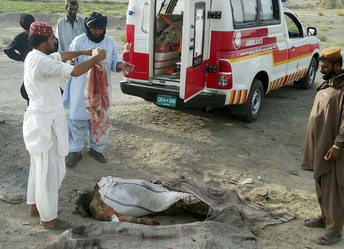 This photo taken by freelance photographer Abdul Malik on May 21, 2016 purports to show volunteers standing next to a dead body by the destroyed vehicle, in which Mullah Mohammad Akhtar Mansour was allegedly traveling in the Ahmed Wal area in Baluchistan province of Pakistan, near Afghanistan border.