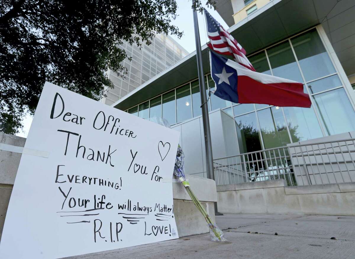 An American flag and a Texas state flag fly at half-staff at San Antonio Police Department headquarters near a sign and flowers left by Lucy Aldaba after Det. Benjamin Marconi was fatally shot Sunday, Nov. 20, 2016 in San Antonio. Marconi was writing out a traffic ticket to a motorist when he was shot to death in his squad car Sunday outside police headquarters by another driver who pulled up from behind, authorities said.