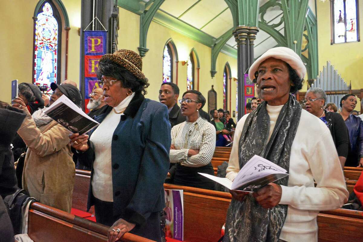 Attendees sing during closing remarks for the Dr. Martin Luther King Day celebration. Many linking arms, community leaders joined other citizens in a procession from Dr. Martin Luther King Jr. Way to the Church of the Holy Trinity.