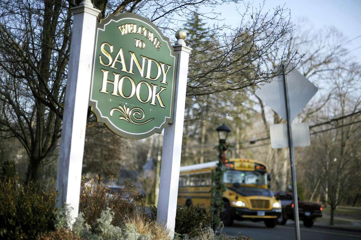In this Dec. 4, 2013, file photo, a school bus drives past a lamppost decorated for the holidays, and a sign reading Welcome to Sandy Hook, in Newtown, Conn. With winter on their doorstep once again, the people of Newtown are bracing for the day everyone there simply calls 12/14 — referring to the day in 2012 with 26 people were killed by a gunman inside Sandy Hook Elementary School.