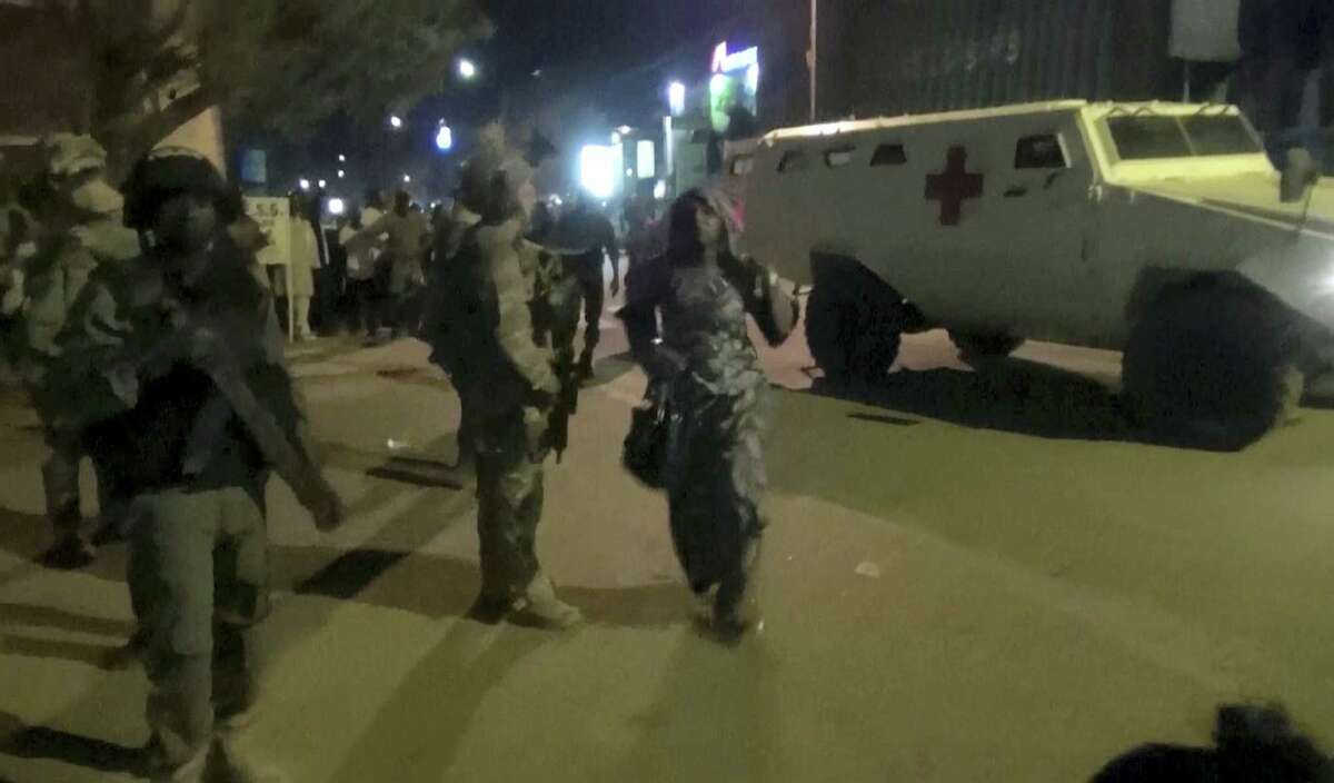In this image taken from video from AP Television, a freed woman, center, walks past French special forces near the Splendid Hotel, early Saturday, Jan. 16, 2016, in Ouagadougou, Burkina Faso. Heavy gunfire erupted early Saturday as forces from Burkina Faso and France worked to overtake the luxury hotel that had been seized by al-Qaida militants the night before.