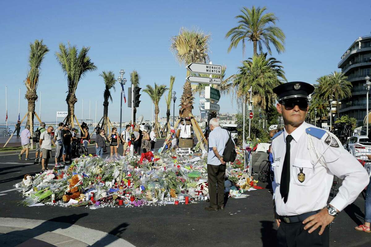 A police officer surveys people gathering around a floral tribute for the victims killed during a deadly attack, on the famed Boulevard des Anglais in Nice, southern France on Sunday, July 17, 2016. French authorities detained two more people Sunday in the investigation into the Bastille Day truck attack on the Mediterranean city of Nice that killed at least 84 people, as authorities try to determine whether the slain attacker was a committed religious extremist or just a very angry man.