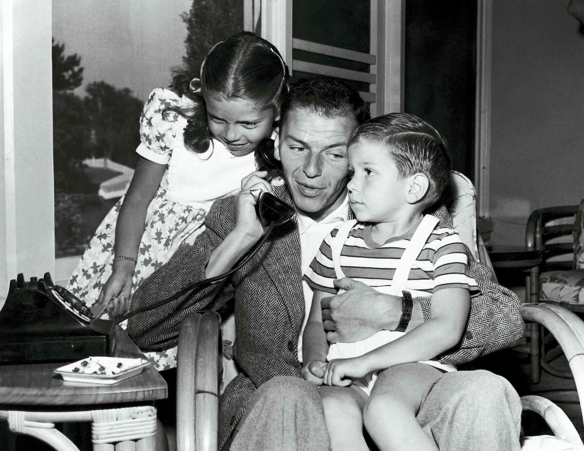 In this 1948 photo, Frank Sinatra holds a telephone with his children, Nancy and Frank Jr., in the Hollywood area of Los Angeles.