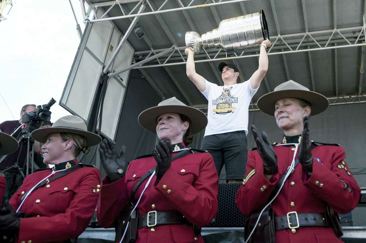 Sidney Crosby hoists the Stanley Cup behind members of the Royal Canadian Mounted Police.