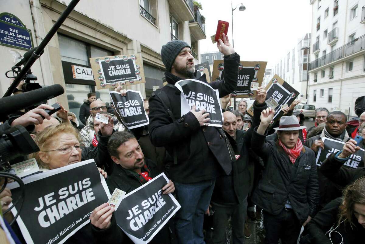 In this Thursday, Jan. 8, 2015, file photo, journalists hold up their press cards during a minute of silence outside the Charlie Hebdo newspaper in Paris, a day after masked gunmen stormed the office. Seventeen people died at Charlie Hebdo on Jan. 7, 2015, and at a kosher supermarket two days later. They were among the first victims of a string of attacks by Islamic fundamentalists in France last year that ultimately left at least 147 people dead and hundreds of others injured. In a special edition marking the anniversary of the Jan. 7 attack on the paper’s staff, Charlie Hebdo’s surviving artists and writers declared that the satirical newspaper is alive, but “the murderer is still at large.”