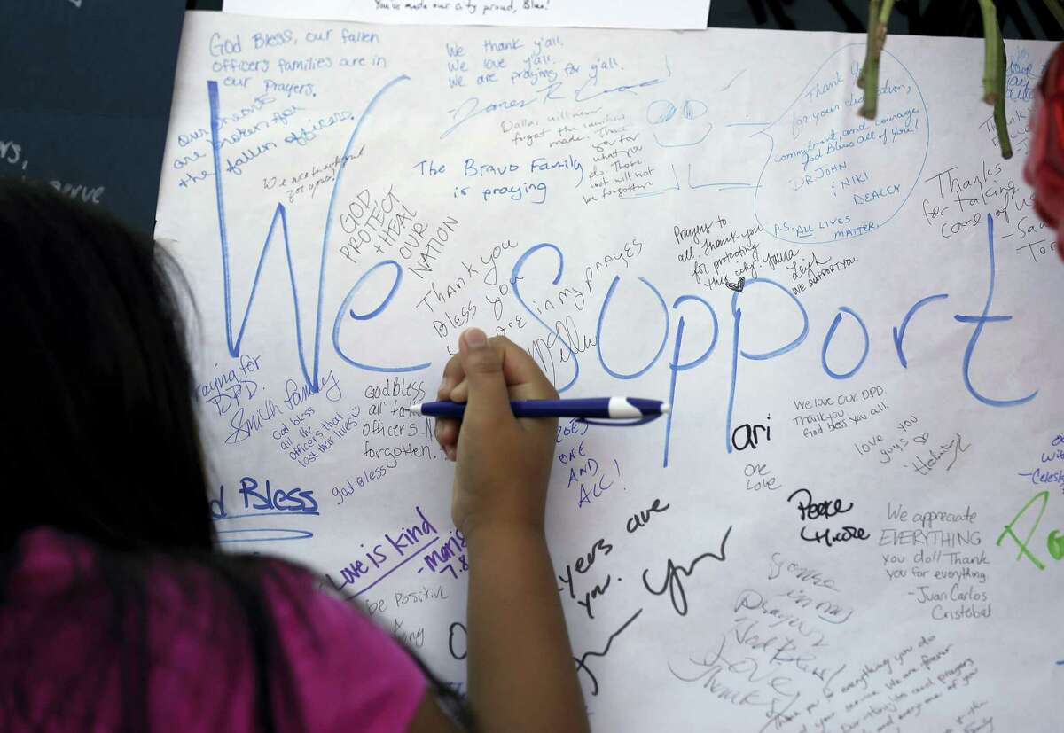 Jasmine Ruiz writes a note at a make-shift memorial in front of the Dallas police department Saturday.