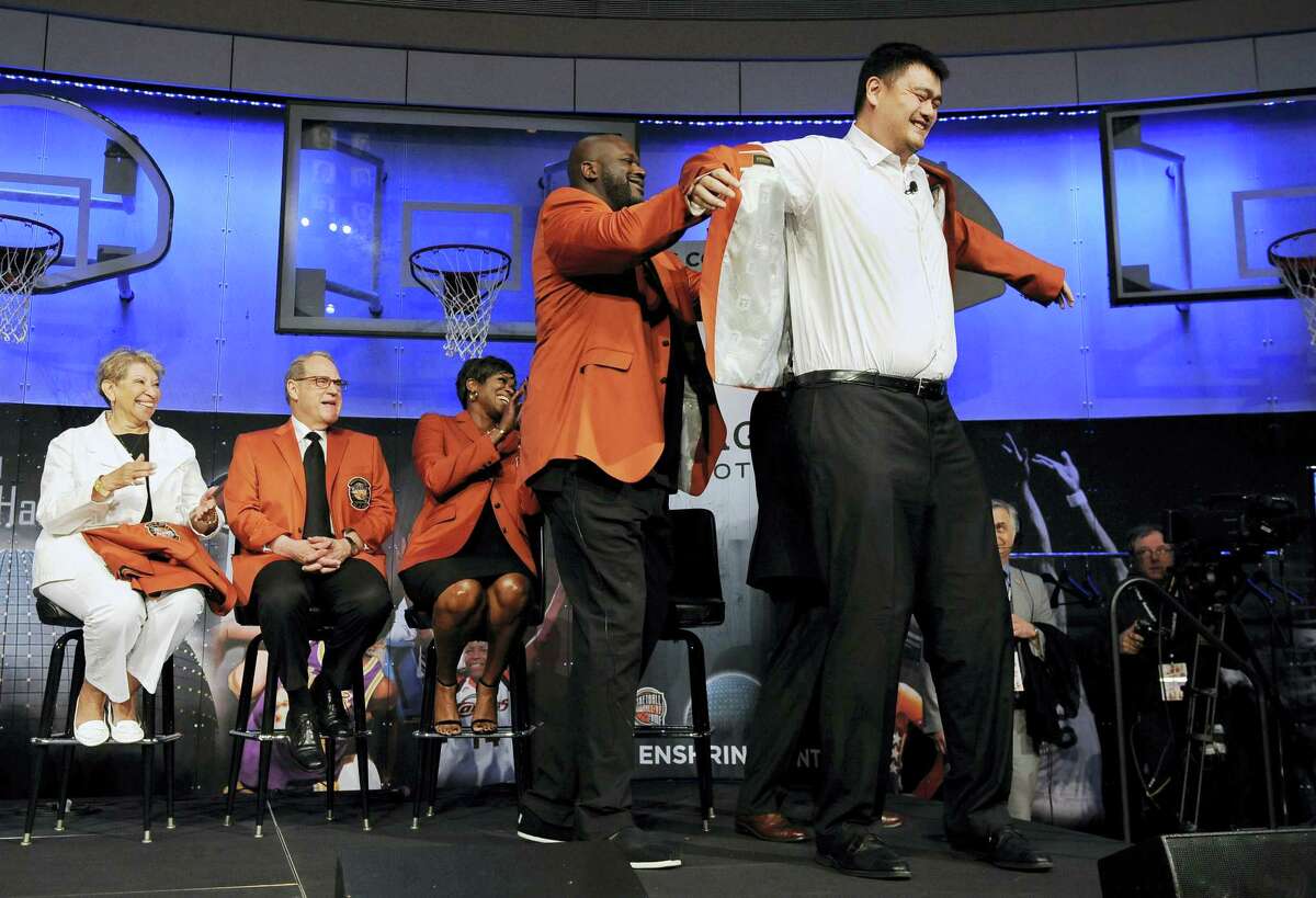 Basketball Hall of Fame inductee Shaquille O’Neal, front left, helps fellow inductee Yao Ming, right, with his jacket during a news conference at the Naismith Memorial Basketball Hall of Fame on Thursday in Springfield, Massachusetts.