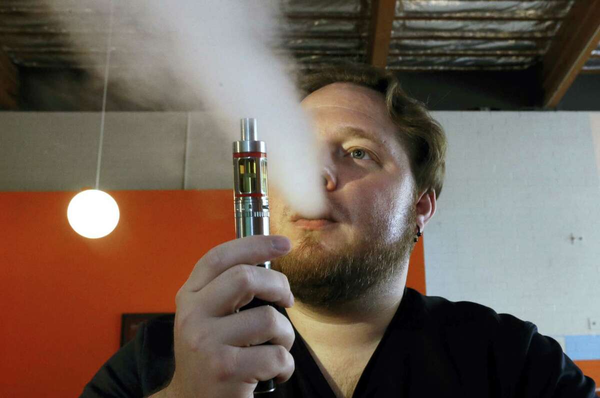 In this July 16, 2015 photo, Bruce Schillin, 32, exhales vapor from an e-cigarette at the Vapor Spot, in Sacramento, Calif.