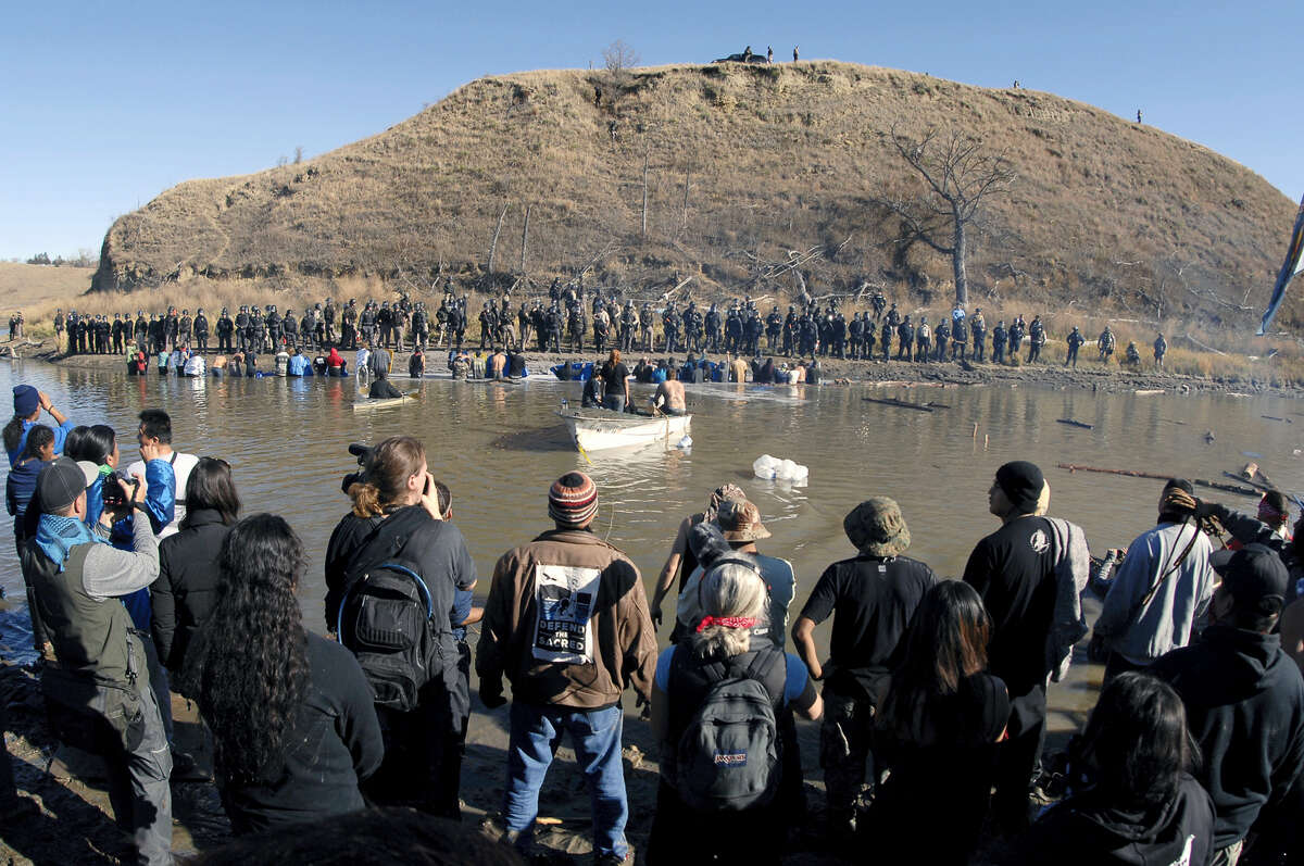 A Dakota Access Pipeline protesters stand in the foreground and in the waist-deep water of the Cantapeta Creek, northeast of the Oceti Sakowin Camp, near Cannon Ball, N.D., Wednesday, Nov. 2, 2016. Officers in riot gear clashed again Wednesday with protesters near the Dakota Access pipeline, hitting dozens with pepper spray as they waded through waist-deep water in an attempt to reach property owned by the pipeline’s developer.