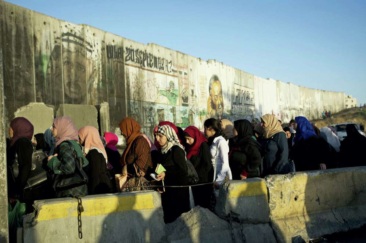 Palestinian women walk past a section of Israel’s separation barrier to cross the checkpoint on their way to attend the third Friday prayers in Jerusalem’s al-Aqsa mosque during Muslim holy month of Ramadan, at the Qalandia checkpoint between the West Bank city of Ramallah and Jerusalem, Friday, June 24, 2016.