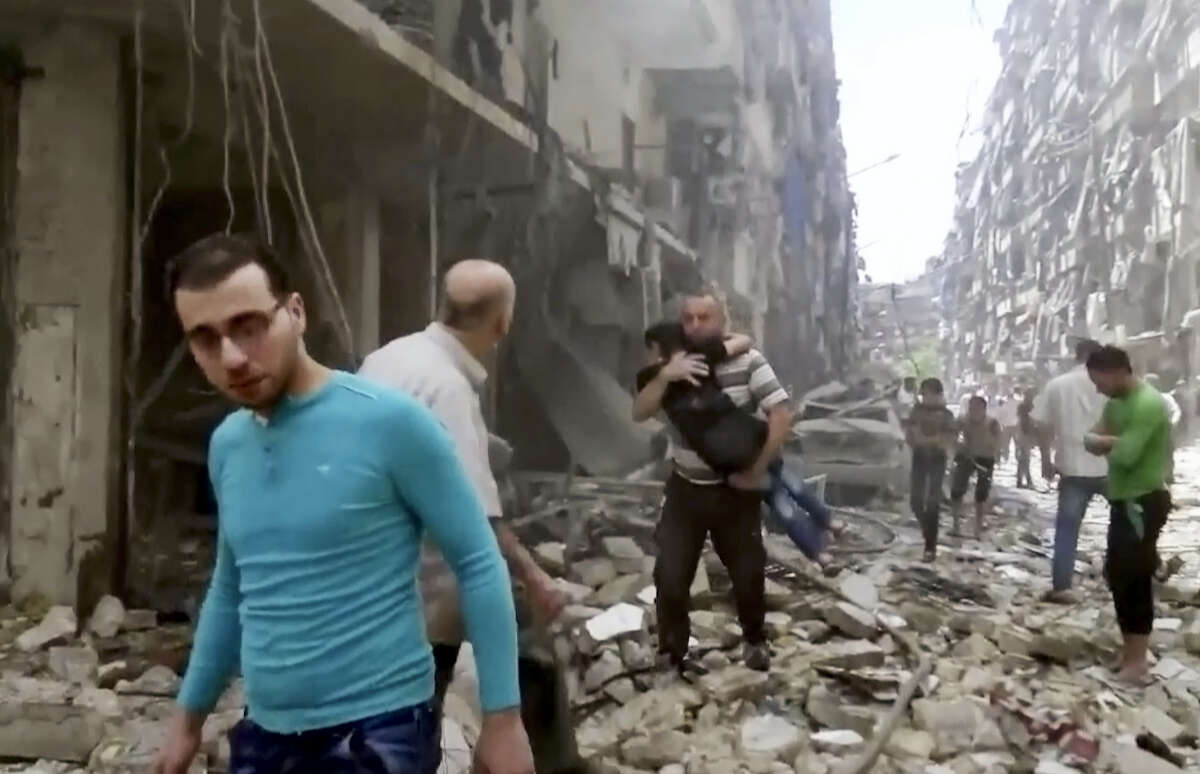 In this image made from video, a man carries a child after airstrikes hit Aleppo, Syria.