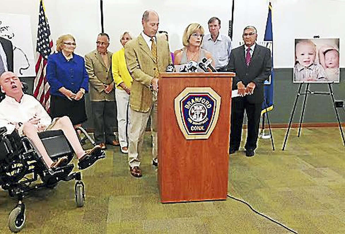 John and Jean Kelley are shown at the podium at the Branford Fire Department on Wednesday with Brian at the left and legislators lined up behind.