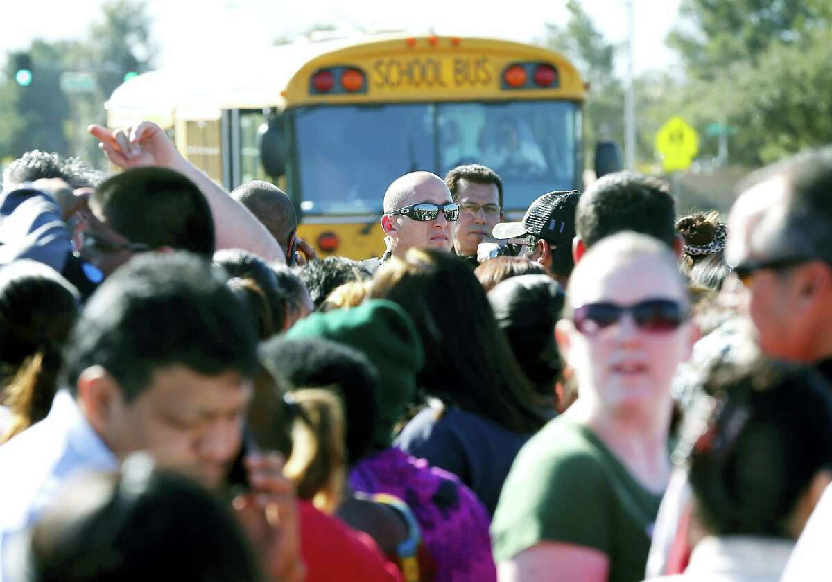 A Phoenix police officer, center, tries to give instructions to parents waiting to board buses to reunite with their children, Friday, Feb. 12, 2016, in Glendale, Ariz., after two students died in a shooting at Independence High School in the Phoenix suburb. The danger at the campus was over, police said, as worried parents crowded stores nearby to await word on their children.