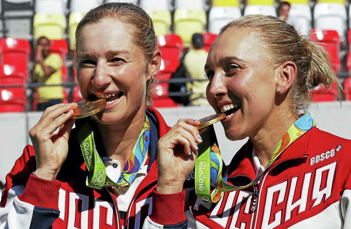 Russia’s Elena Vesnina, right, and Ekaterina Makarova nibble on their gold medals in Rio.