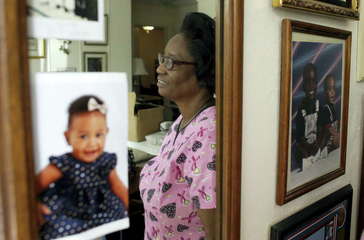 In this photo taken Oct. 18, 2016, Gwen Strowbridge, 71, poses for a photograph among photos of her grandchildren wearing her work uniform at her home in Deerfield Beach, Fla. Strowbridge works six days a week caring for a 100-year-old woman. She has worked all her life and plans to work until she can’t physically work anymore.