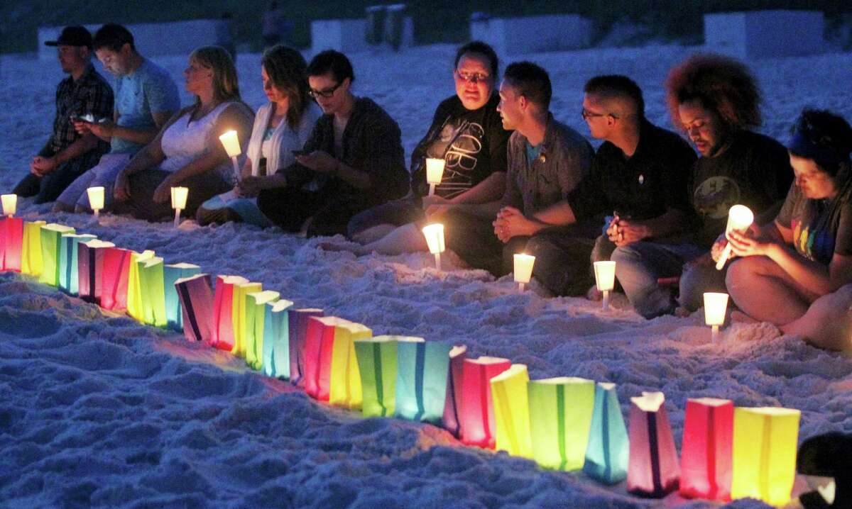 People sit near a row of lumenaria during a candle light vigil for those killed in the Orlando Night Club shooting that was held Thursday, June 16, 2016 in the Florida panhandle community of Santa Rosa Beach.