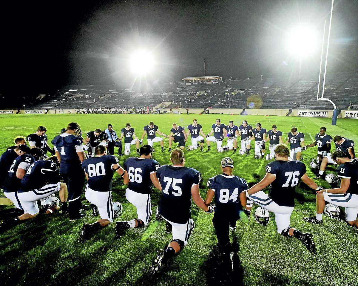 Members of the Yale football kneel for prayer before the first night football game at Yale Bowl on Friday.
