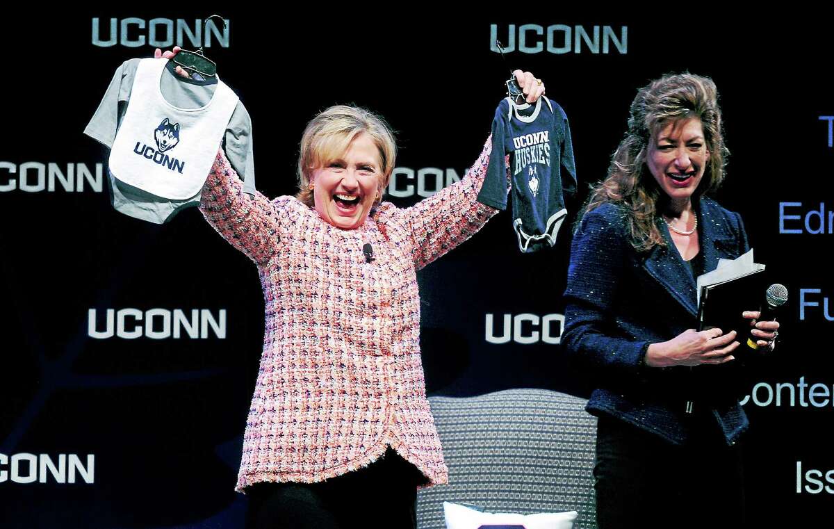 Former Secretary of State Hillary Clinton (left) shows off onesies given to her by University of Connecticut president Susan Herbst at the Edmund Fusco Contemporary Issues Forum at UCONN on 4/23/2014. Clinton was expecting a grandchild at that time.