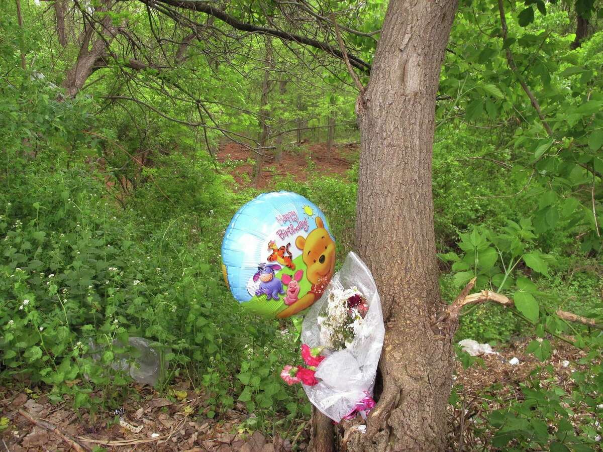 A happy birthday balloon and flowers left for one of seven victims of a suspected serial killer are tied to a tree in New Britain, Conn., on May 12, 2015. A clearing in the woods seen just above the balloon is one area of the woods where the remains of the seven victims were found in 2007 and last month.