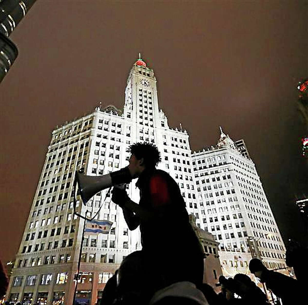 A protester is silhouetted against Chicago’s famed Wrigley Building as he directs others to shutdown traffic on both sides of the Michigan Ave. bridge over the Chicago River, Wednesday, Nov. 25, 2015, one day after murder charges were brought against police officer Jason Van Dyke in the killing of 17-year-old Laquan McDonald.