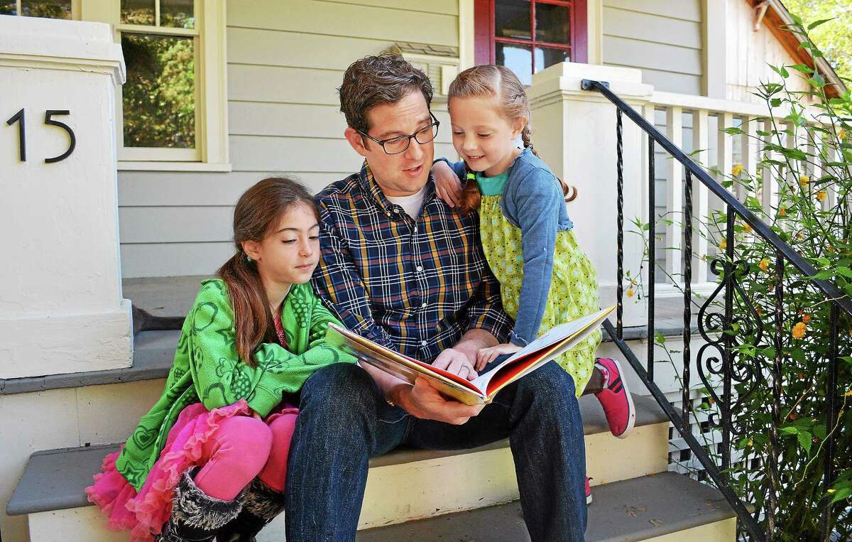 Catherine Avalone — The Middletown Press Jeff Cohen, a public radio reporter at WNPR 90.5-FM, is the author of a children’s book, “Eva and Sadie and the Worst Haircut EVER!” Cohen reads the book to his daughters, Sadie, 8, left and Eva, 6, on the porch of their Middletown home Friday morning. The book is based on a true story about the time Sadie cut her little sister’s hair.