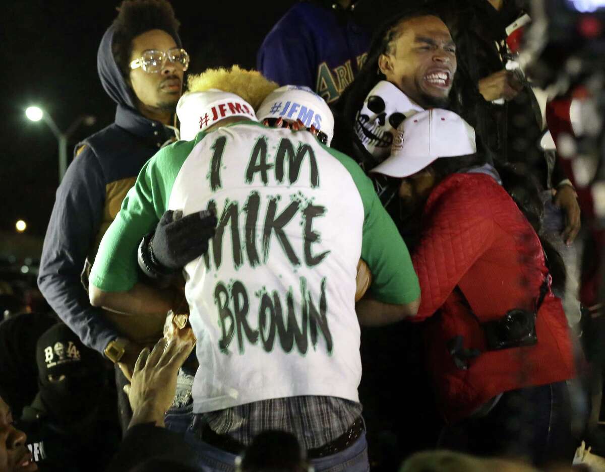 Lesley McSpadden, the mother of Michael Brown, second from left standing on the top of a car, hugs an unidentified man, wearing an I am Mike Brown shirt, as she listens to the announcement of the grand jury decision Monday, Nov. 24, 2014, in Ferguson, Mo. A grand jury has decided not to indict Ferguson police officer Darren Wilson in the death of Michael Brown, the unarmed, black 18-year-old whose fatal shooting sparked sometimes violent protests.