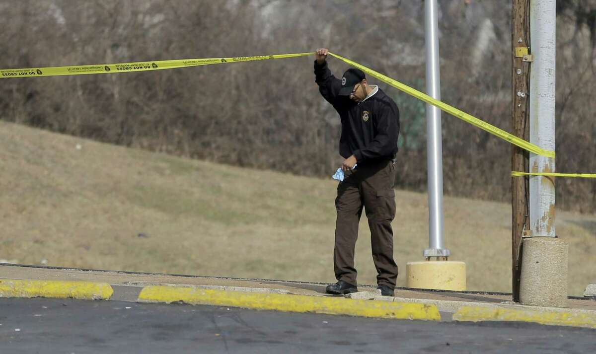 An investigator lifts crime scene tape near the Ferguson Police Department Thursday, March 12, 2015, in Ferguson, Mo. Two police officers were shot in front of the police department early Thursday as demonstrators gathered after the police chief resigned in the wake of a scathing Justice Department report alleging bias in the police force and local courts. (AP Photo/Jeff Roberson)
