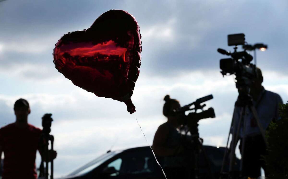 Reporters gather around a memorial of balloons and flowers placed outside of WDBJ7’s Digital Broadcast Center in Roanoke, Va., Wednesday, Aug. 26, 2015. The shooting of a television reporter and a cameraman unfolded on live TV before an audience of tens of thousands on the smaller market central Virginia television station.