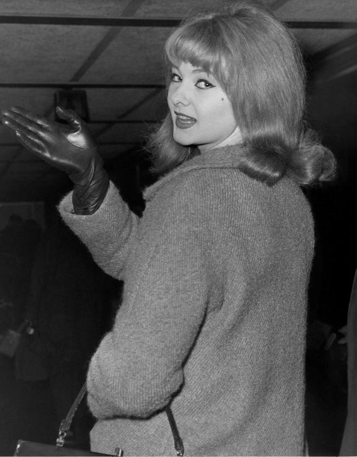 FILE - In this Jan. 7, 1964 file photo, Mandy Rice-Davies waves goodbye at London Airport as she leaves for Munich for a singing engagement. Mandy Rice-Davies, a key figure in Britain’s biggest Cold War political scandal, the ìProfumo Affair,î has died. She was 70. Her PR firm said Friday Dec. 19, 2014, that Rice-Davies died Thursday evening “after a short battle with cancer.”