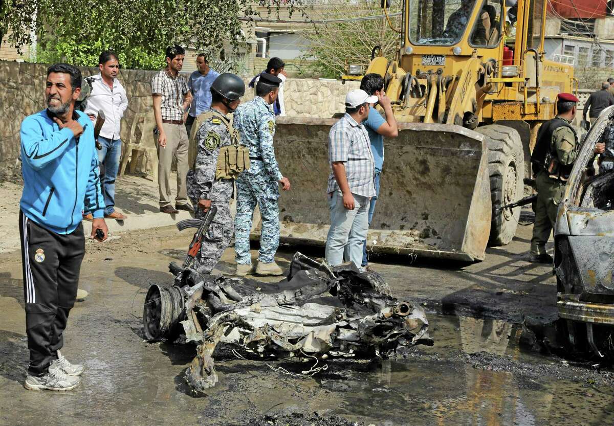 A municipality bulldozer cleans up while Iraqi security forces and others gather at the site of a car bomb attack in Baghdad, Iraq, Wednesday, March 5, 2014. A series of car bombs hit Wednesday in commercial areas of Baghdad, that killed and wounded scores of people, according to Iraqi officials. (AP Photo/Karim Kadim)