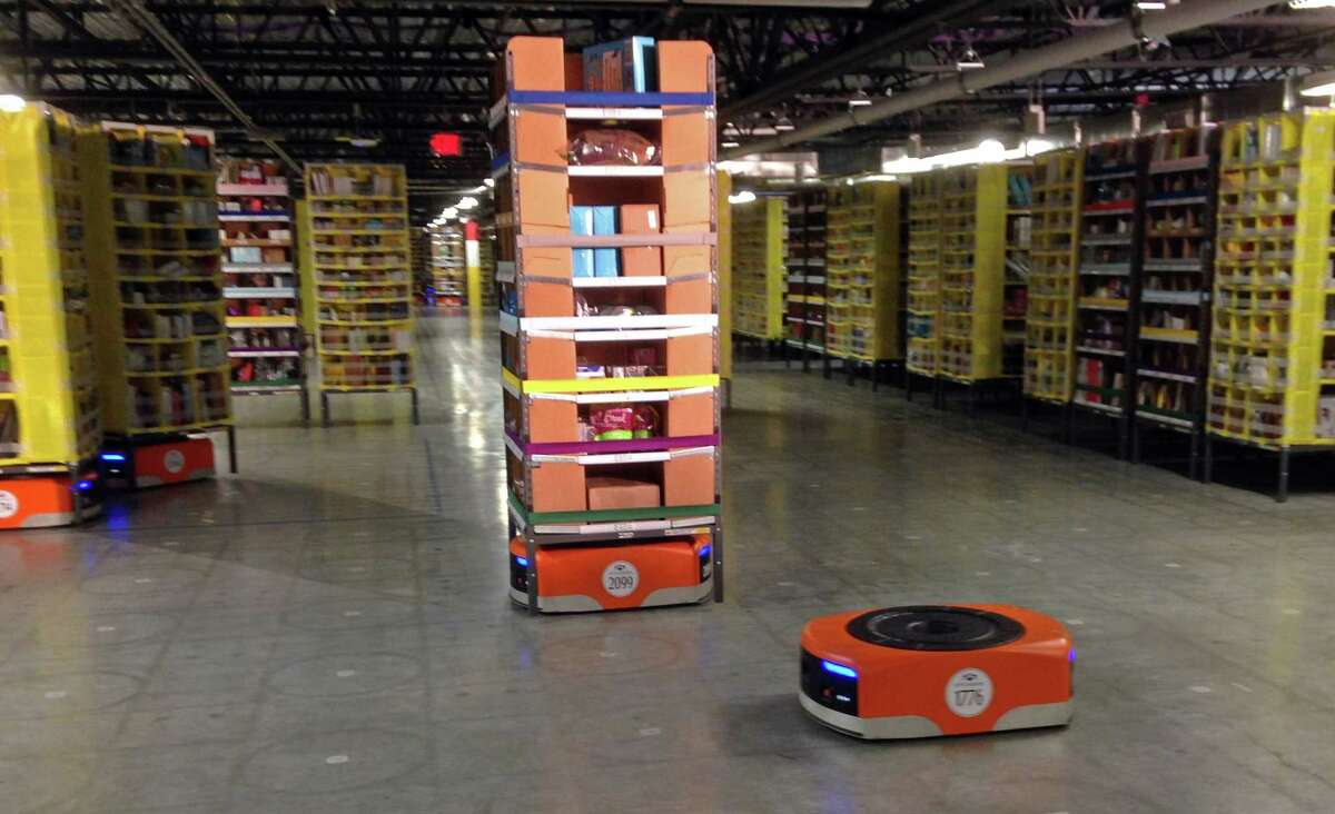A Kiva robot drive unit is seen, foreground, before it moves under a stack of merchandise pods, seen on a tour of one of Amazon’s newest distribution centers in Tracy, Calif., Sunday.