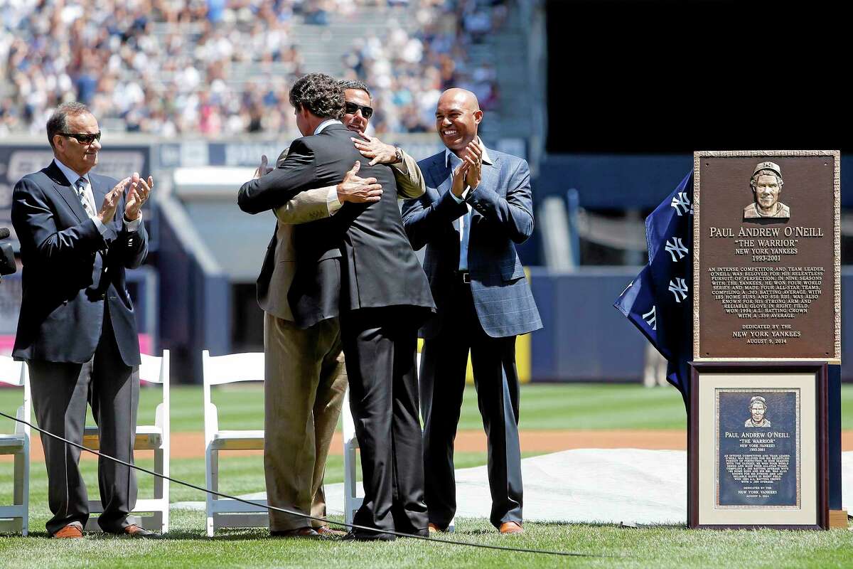 Former Yankee Paul O’Neill, center facing away, is congratulated by former manager Joe Torre, left, and former teammates Jorge Posada, embracing, and Mariano Rivera after unveiling a plaque, right, that will be displayed in Yankee Stadium’s Monument Park.