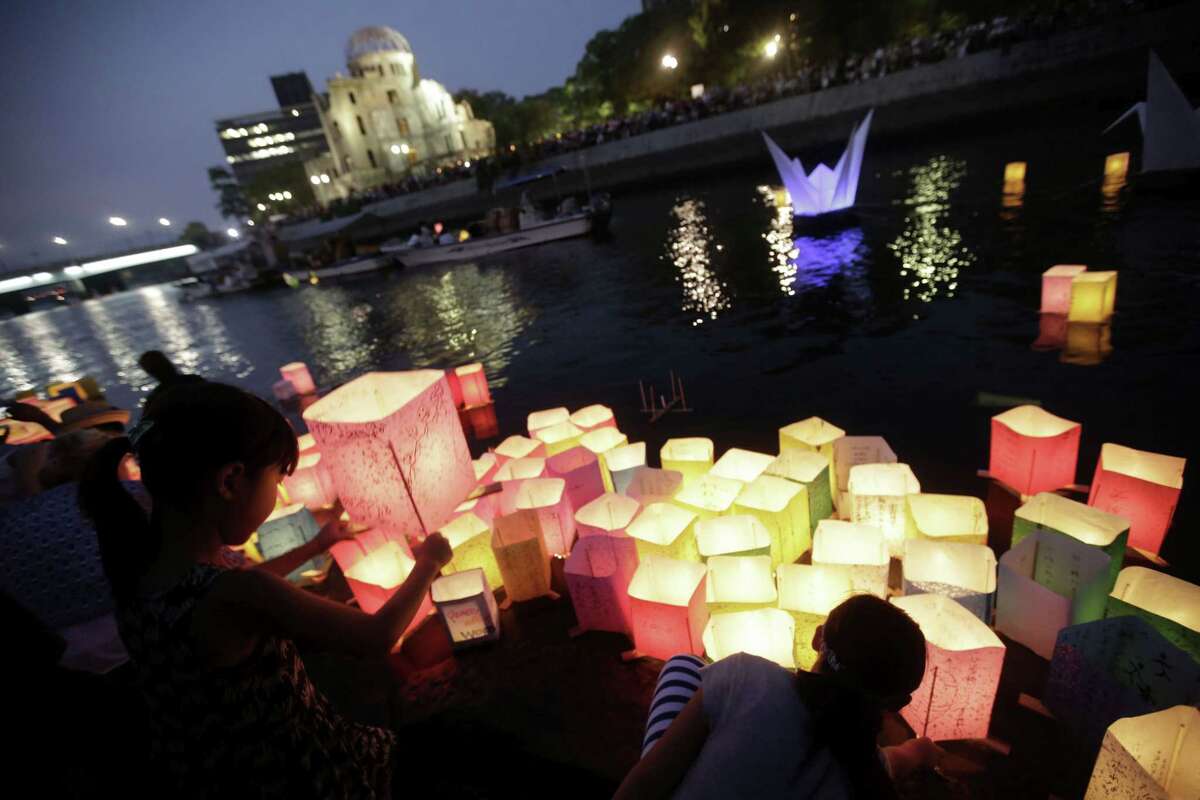 Children offer prayers after releasing paper lanterns on the Motoyasu River where hundreds of thousands of atomic bombing victims died with the backdrop of the Atomic Bomb Dome in Hiroshima, western Japan, Thursday, Aug. 6, 2015.