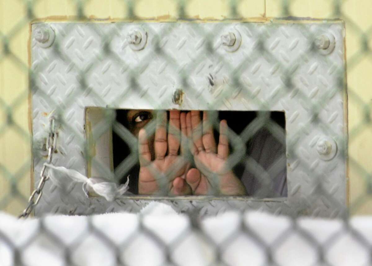 In this Dec. 4, 2006, file photo, a detainee shields his face as he peers out through the so-called “bean hole” at Camp Delta detention center, Guantanamo Bay.