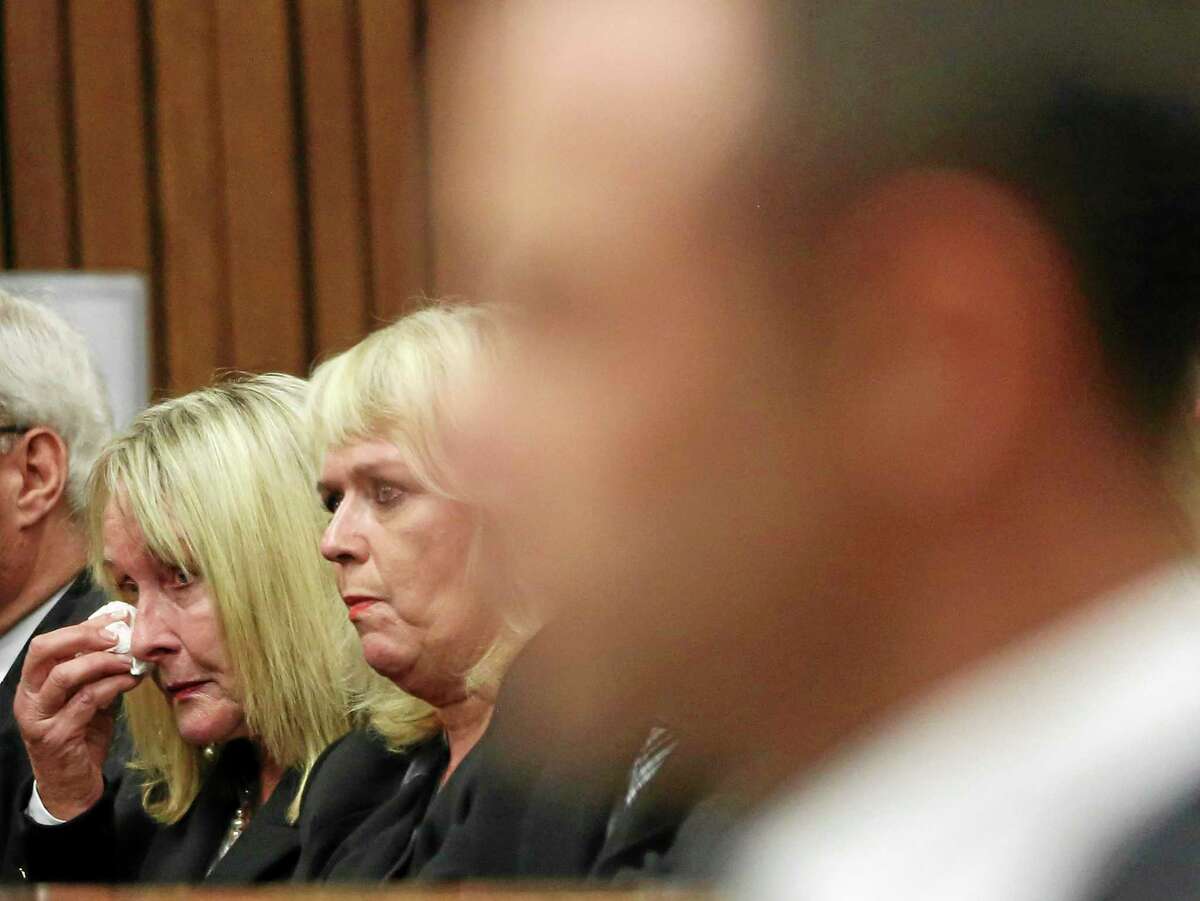 June Steenkamp, the mother of Reeva Steenkamp, left, wipes her face with a tissue at the start the trial of Oscar Pistorius, right, at the high court in Pretoria, South Africa, Monday, March 3, 2014. Pistorius pleaded not guilty Monday to murdering his girlfriend on Valentine's Day last year, marking the start of the Olympian's murder trial that had South Africans watching live broadcasting of the proceedings against their country's most famous living citizen. (AP Photo/Themba Hadebe, Pool)
