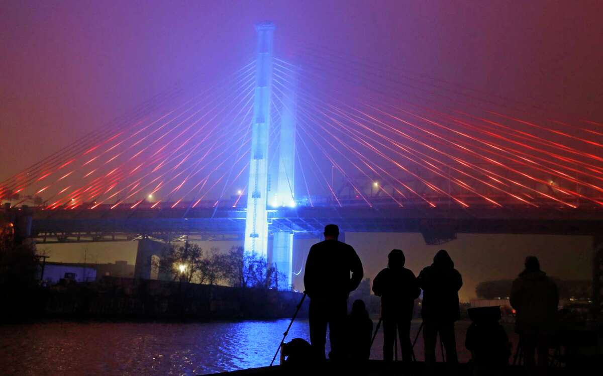 FILE - In this April 27, 2017, file photo, spectators and photographers linger after a performance of the "New York Harbor of Lights" at the grand opening of the new Kosciuszko Bridge span connecting Brooklyn and Queens, in New York. Gov. Andrew Cuomo liked the idea of stringing New York City's bridges with high-tech lights that change color and pulsate to the beats of Broadway showtunes. But the plan, meant to delight tourists and residents alike, is sputtering amid criticism that the money for the lights should have gone to the city's beleagured subway system. (AP Photo/Kathy Willens, File) ORG XMIT: NYR201