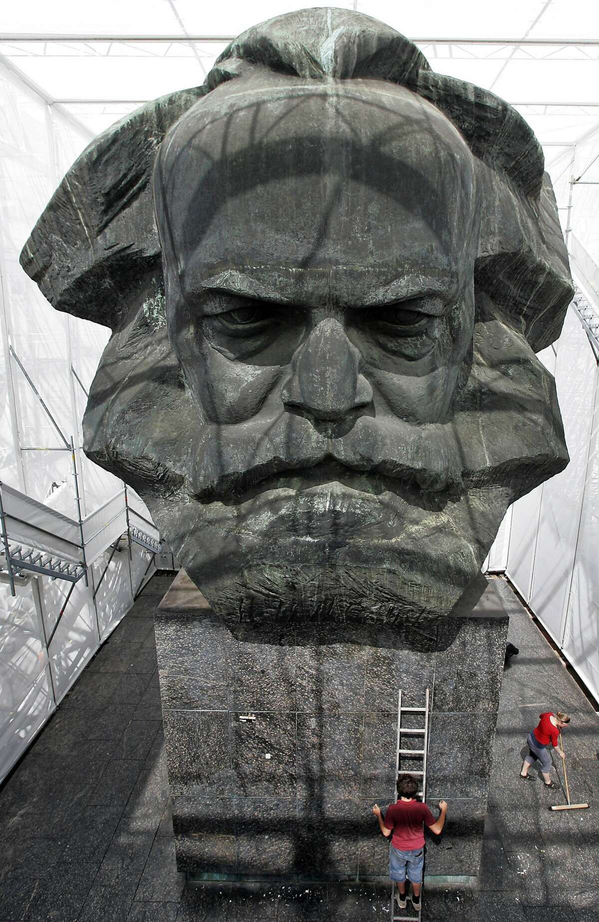 Workers clean up at the so-called "Temporary Museum of Modern Marx" walk on the steps past the plastic bust sculpture of German communist theorist Karl Marx in eastern German city of Chemnitz on June 17, 2008. The 13-meter sculpture by Soviet artist Lew Kerbel was unveiled in 1971 in the city then known as Karl-Marx-Stadt, has now been enclosed in a tent like covering by students of the art college in Linz, Austria. AFP PHOTO DDP / UWE MEINHOLD GERMANY OUT (Photo credit should read UWE MEINHOLD/AFP/Getty Images)