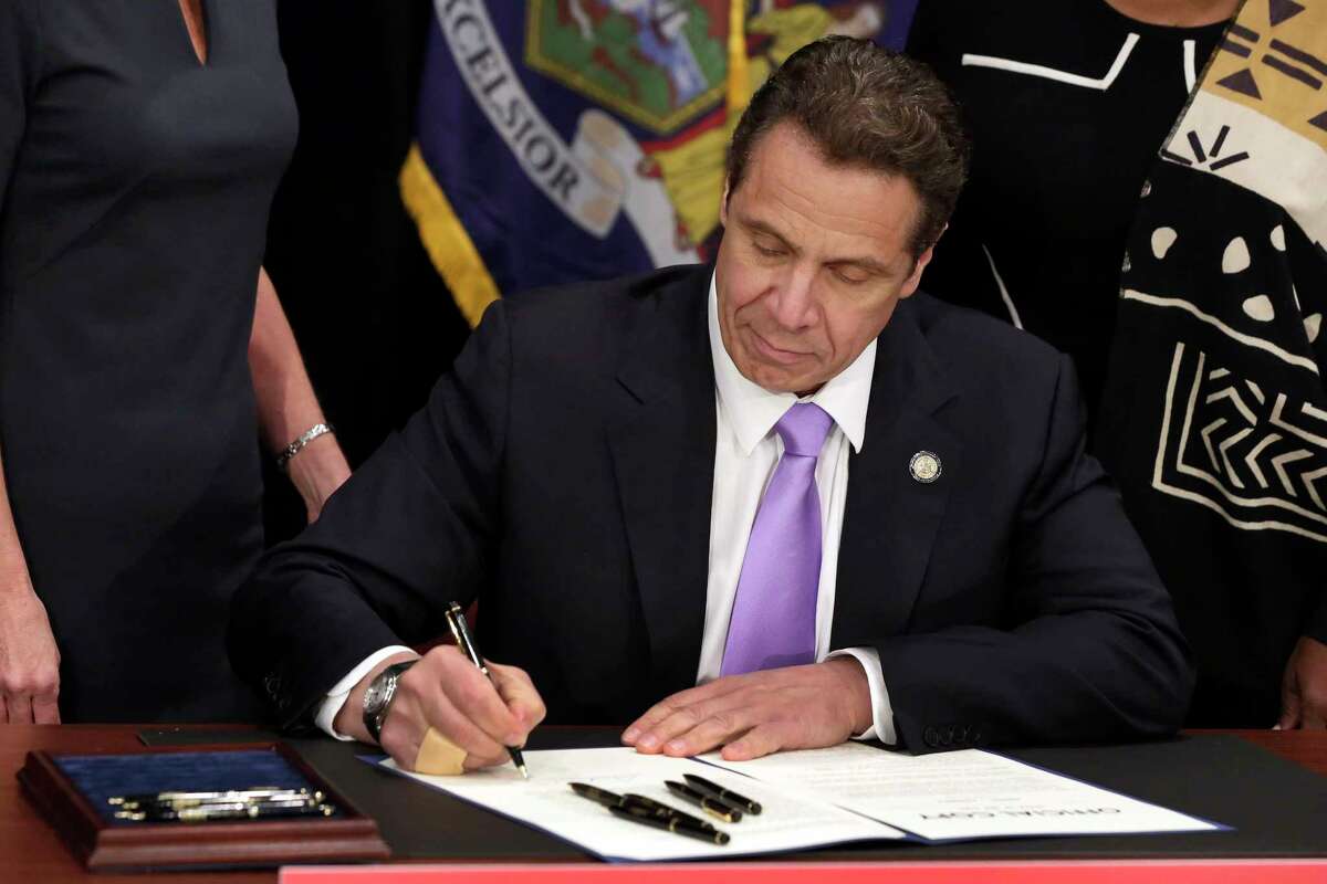 FILE- In this April 4, 2016 file photo, New York Gov. Andrew Cuomo signs a law that will gradually raise New York's minimum wage to $15. On Dec. 17, 2017, Cuomo said he would convene a panel to look at the tipped wage. (AP Photo/Richard Drew, Pool, File)