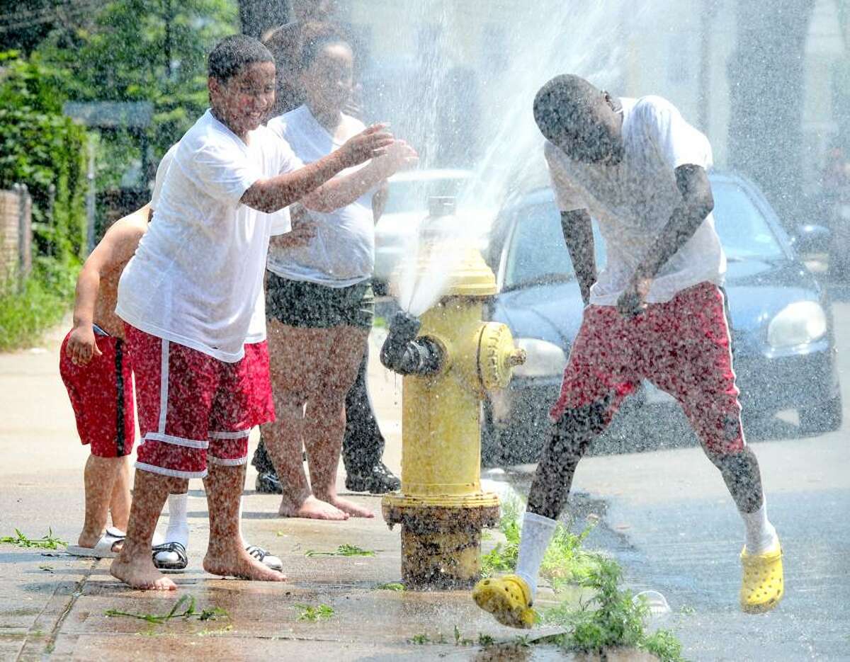 Kevin Wilfong, right, runs through the water coming out of a sprinkler on a fire hydrant on Button Street in New Haven. At left is Christopher Carrero. (File photo)