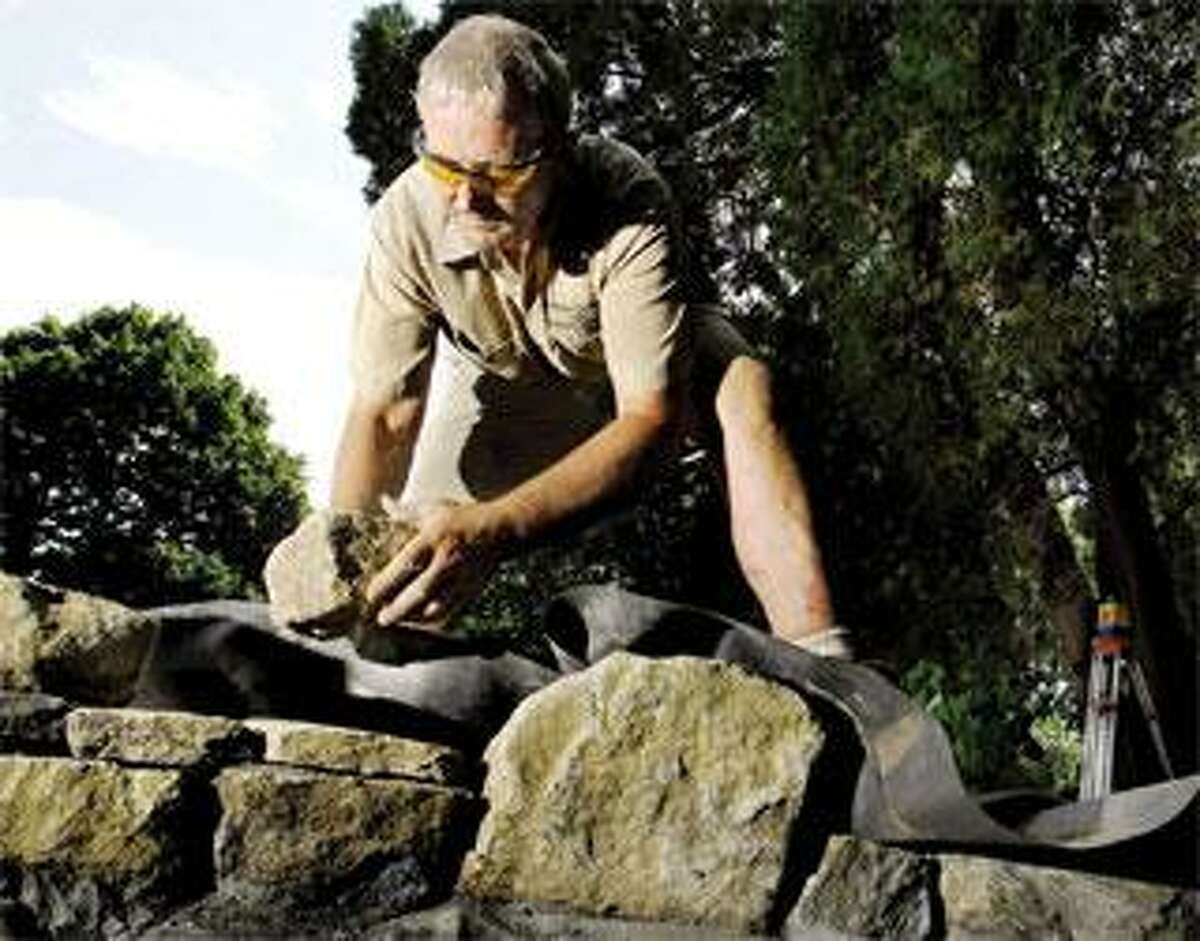 Stone wall craftsman Andrew Pighills builds a mortared stone wall for a pond at a Madison house. (Peter Hvizdak/Register)