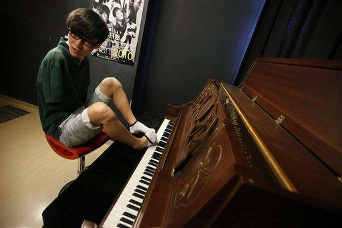 FILE - In this Aug. 26, 2010 file photo, pianist Liu Wei takes off one of his socks to play a piano before his practice session in Shanghai. The musician who lost both arms in a childhood accident and plays the piano with his toes won "China's Got Talent," performing his version of James Blunt's wistful lovesong "You're Beautiful" to a packed audience at the Shanghai Stadium, on Sunday, Oct. 10, 2010. (AP Photo/Eugene Hoshiko, File)