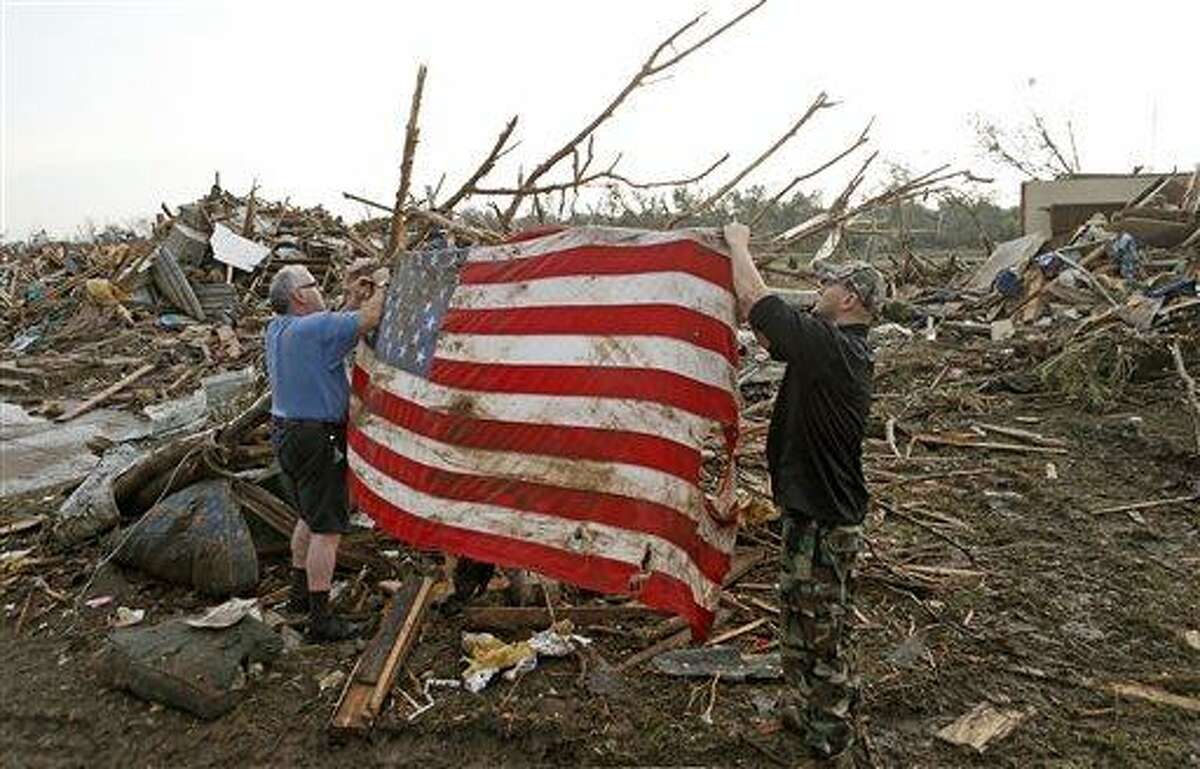 Clark Gardner, at left, and another man place an American flag on debris in a neighborhood off of Telephone Road in Moore, Okla., after a tornado moved through the area on Monday, May 20, 2013. (AP Photo/ The Oklahoman, Bryan Terry)