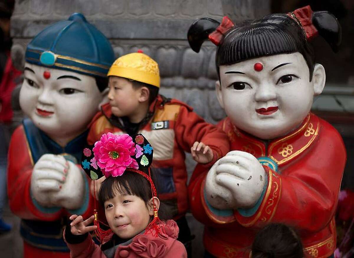 Children wearing traditional Chinese hats pose with a pair of statues on display at a shopping district in Beijing Thursday, Feb. 14, 2013. (AP Photo/Andy Wong)