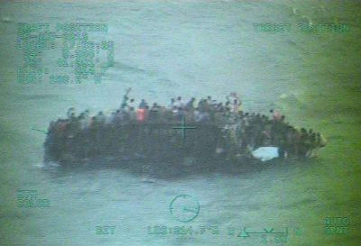 This image taken from video made available by the U.S. Coast Guard shows a group of Haitian migrants sitting on the hull of a capsized sailboat near Staniel Cay, Bahamas on Nov. 26, 2013.