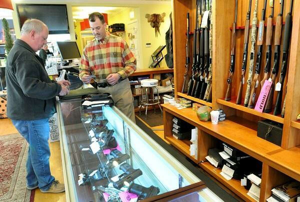 Thomas Powers of Branford, left, shows his pistol permit to Mike Higgins, co-owner of TGS Outdoors on Main Street in Branford, Conn. as they start the required Federal and State of Connecticut paperwork before he purchases a handgun there Tuesday April 2, 2013. Photo by Peter Hvizdak / New Haven Register.