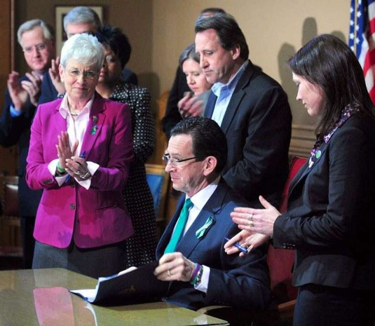 Lt. Governor Nancy Wyman (left), Neil Heslin (top center) and Nicole Hockley (right) applaud as Governor Dannel Malloy (center bottom) completes the signing the Gun Violence Prevention and Child Safety Act at the Capitol in Hartford on 4/4/2013. Photo by Arnold Gold/New Haven Register